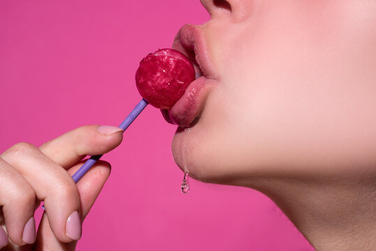 Orgasm concept. Lollipop in the mouth, close-up. Beautiful girl mouth with lolli pop. Glossy red woman lips with tongue. Mouth lick suck chupa chups isolated on pink.