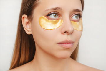 Close-up of a young pretty caucasian blonde woman with gold patches on the skin under her eyes looking away isolated on a white background. Skin care, cosmetology