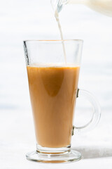 milk is poured into a glass cup with coffee, closeup