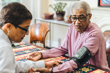 Elderly woman looks at her arm while her adult daughter checks her blood pressure