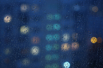 raindrops on the glass of the window against the background of house lights in the evening in autumn