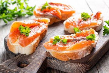 Slices of fresh baguette with butter and salmon served on wooden board on wood table
