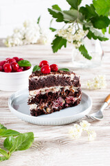 A slice of black chocolate sponge cake with cherry on a wooden table