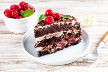 A piece of chocolate cake with cherry on plate on a wooden table.