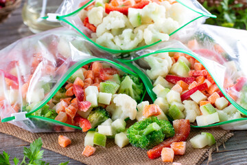 Plastic bags with different frozen vegetables on a wooden table