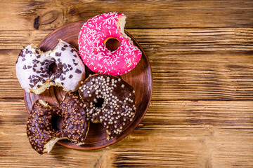 Plate with bitten glazed donuts on a wooden table. Top view