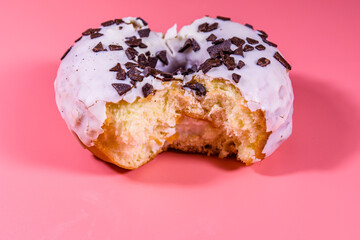 Bitten glazed donut with chocolate chip on top isolated on a pink background