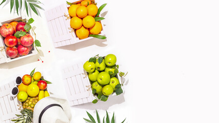 Summer tropical fruits. Horizontal banner with oranges, apples, pomegranates and pineapple in white wooden boxes on a white background with copy space. Local market. Harvest Day. Summer sale of fruits