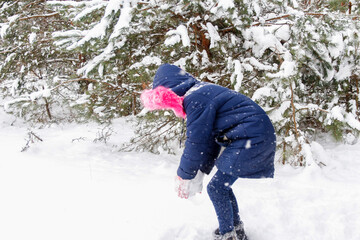Fototapeta na wymiar Preteen child girl in winter forest in snowstorm. Kid on snowy winter background playing snowball. Actively spending time outdoors. Winter woodland. Cold frost weather in snowstorm. Happy childhood