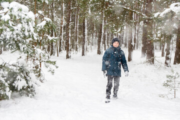 Front view of child boy in winter forest in snowstorm. Kid on snowy winter background. Actively spending time outdoors. Winter snowy woodland. Cold frost weather in snowstorm. Happy childhood