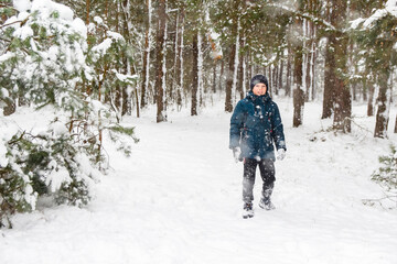 Smiling child boy in winter forest in snowstorm. Kid on snowy winter background. Actively spending time outdoors. Winter snowy woodland. Cold frost weather in snowstorm. Happy childhood