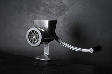 Metal manual meat grinder on dark table against black background