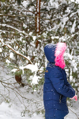 Portrait of little happy girl in pink warm fur hood walking outside on nature winter snowy forest background. Pretty child outdoor, cold weather. Caucasian kid. Winter nature. Vertical. Side view