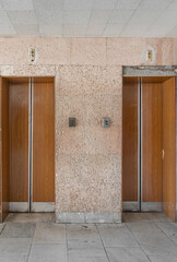 Closed old Soviet wooden elevator doors in the old interior in the style of modernism, with walls lined with travertine.