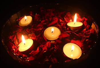 Tea light candles and red rose petals floating on water filled in a transparent glass bowl