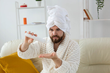 Bearded man holds white bottle cream or gel for skin care. Spa, body and skin care for man concept