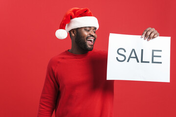 Black man in christmas hat laughing while showing sale placard