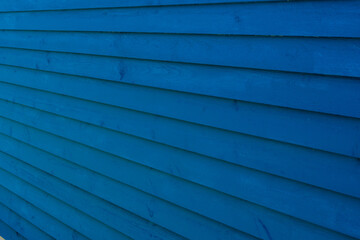 The exterior wall of a bright blue building. The textured wood is made of pine clapboard and the board is horizontal on the house. The backdrop of yellow lines is both a clean and modern style house.