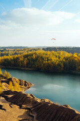 A young man flies and glides on a paramotor with a red wing over an autumn forest and a river. The weather is sunny. Preparation for paramotor flights. Below is a beautiful landscape.