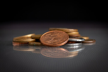 moedas empilhadas em superfície de vidro, refletindo no vidro, em um fundo escuro, com o foco em uma moeda de 5 centavos de BRL. 