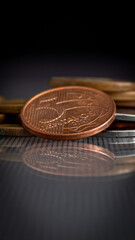 moedas empilhadas em superfície de vidro, refletindo no vidro, em um fundo escuro, com o foco em uma moeda de 5 centavos de BRL. 