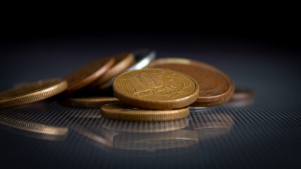 moedas empilhadas em superfície de vidro, refletindo no vidro, em um fundo escuro, com o foco em uma moeda de 10 centavos de BRL. 