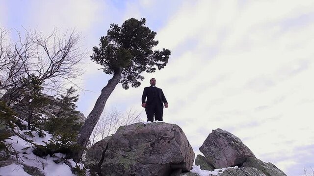 the priest preaches on the mountain. A man in the clothes of a pastor stands on a stone. Winter and cold in the mountains