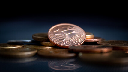 moedas empilhadas em superfície de vidro, refletindo no vidro, em um fundo escuro, com o foco em uma moeda de 5 centavos de BRL. 