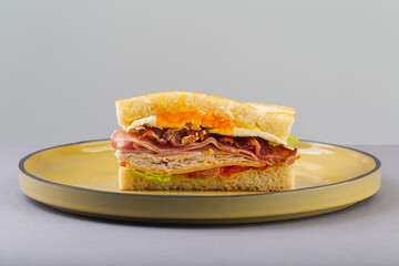 Breakfast sandwich with egg, bacon and vegetables on grey close-up