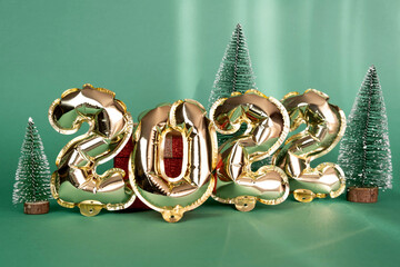 Golden balloons of 2022, miniature Christmas trees isolated on a mint-colored background. Helium balloons, gold foil numbers. Figures for a Happy New Year 2022. Decoration of parties, celebrations.