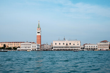 Fototapeta na wymiar Doge's palace and Campanile on Piazza di San Marco, Venice, Italy with reflection. View from passing vaporetto boat, with sea water of Venice Lagoon in front.