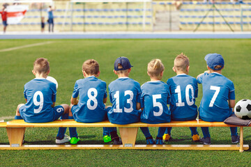 School Boys in Sports Football Team. Kids is Classic Blue Soccer Jersey Uniforms With Numbers. Kids Playing Sports Together. Children Sitting on Sideline Wooden Substitiute Bench