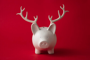 Christmas saving money box wearing festive reindeer antlers. Seasonal finance background