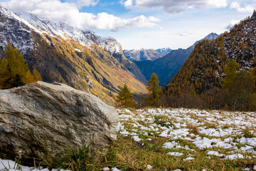Alpine valley in autumn after a small snowfall. Rock in the foreground.