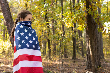 Little girl hides her face under big American flag. 