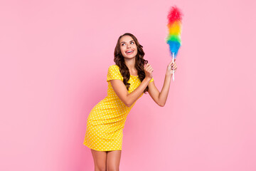 Photo of pretty dreamy young woman wear yellow dress smiling looking empty space cleaning dust isolated pink color background