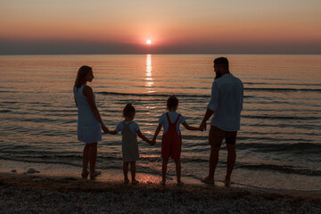 big family on the beach. Silhouettes of people against the sunset. 4 people holding hands