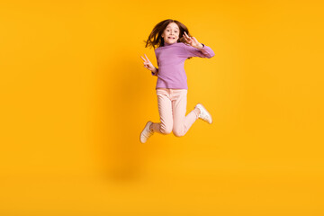 Fototapeta na wymiar Full size photo of happy excited positive smiling little girl jumping show v-sign isolated on yellow color background