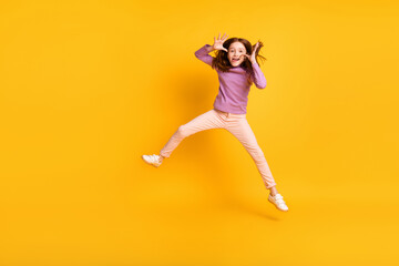 Full size photo of funky funny humorous little girl jumping fooling around showing tongue isolated on yellow color background