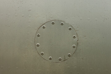 Round hatch with rivets of an old camouflage surface with green color on a military aircraft. Fragment of a fuselage of an old jet fighter