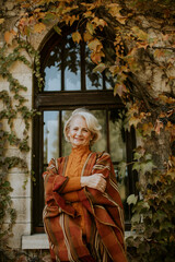 Senior woman standing by the window at the autumn day