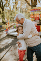 Grandfather having fun with his little granddaughter in the amusement park