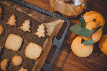Christmas gingerbread cookies in the form of fir trees on a pan next to oranges on a wooden table.
