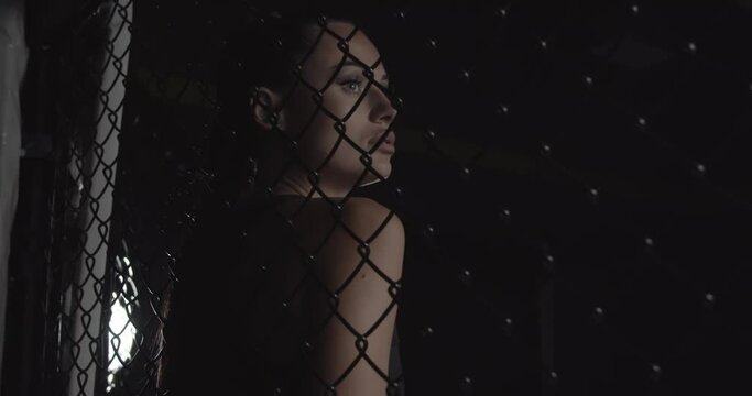 Modern fashionable woman behind a tatami net in the dark with a lighted face looking at the camera. Sports topics. Contour light