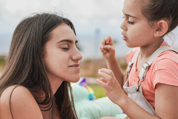 Cute little girl making up her big sister with glitter eye shadow at home outdoor in the garden