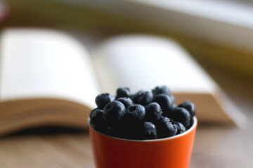 Cup filled with blueberries and open book on a table. Selective focus.