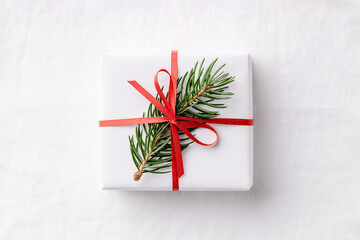One white Christmas gift box with fir branch on white linen tablecloth.