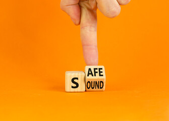 Safe and sound symbol. Businessman turns a wooden cube and changes the word 'safe' to 'sound' or vice versa. Beautiful orange table, orange background, copy space. Business, safe and sound concept.