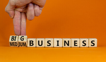 Big or medium business symbol. Businessman turns wooden cubes, changes words medium business to big business. Beautiful orange background, copy space. Big or medium business concept.