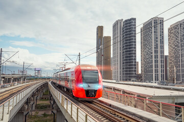 Electric passenger train drives at high speed among modern urban landscape.